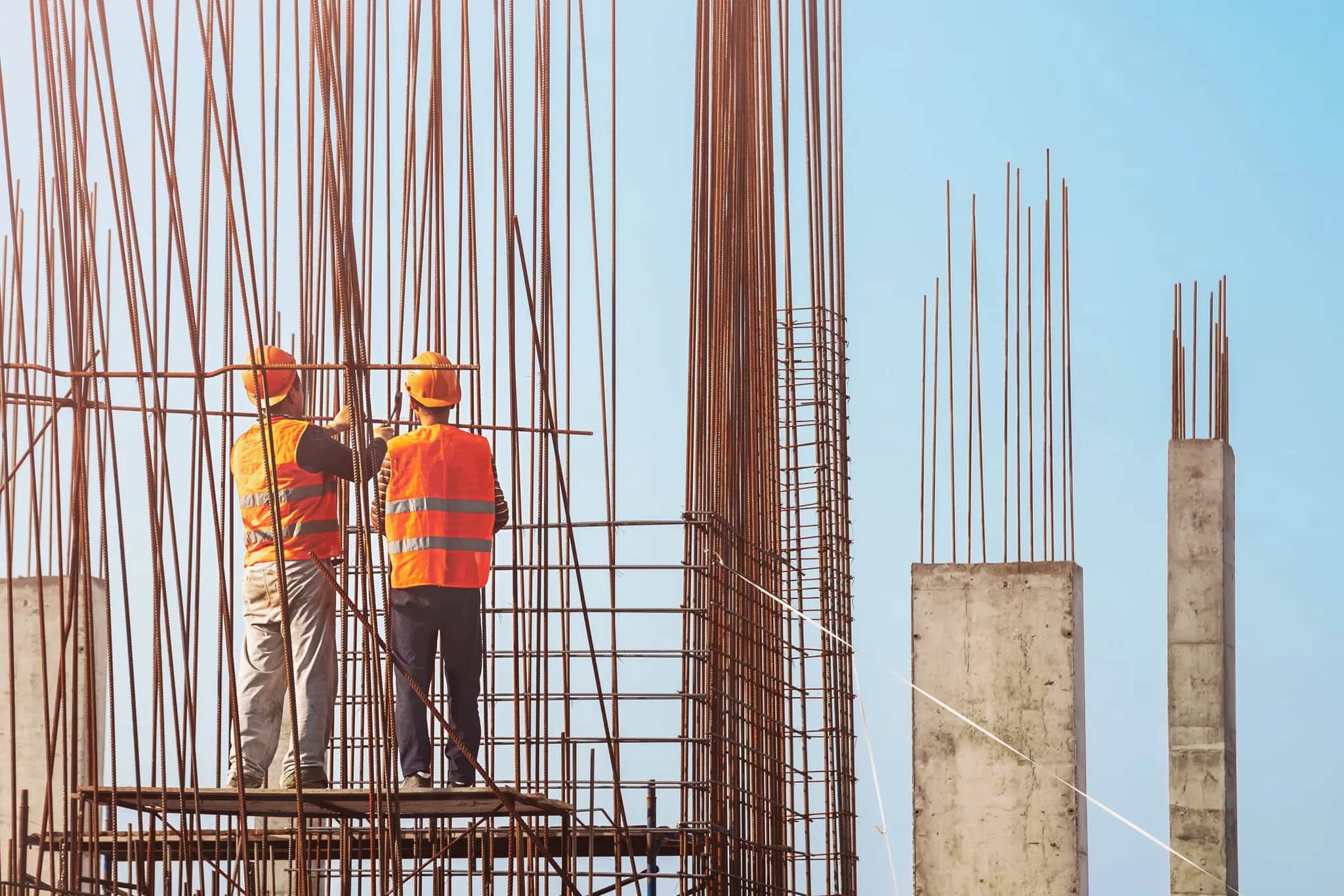 Two workers among vertical reinforcement columns on a structural site