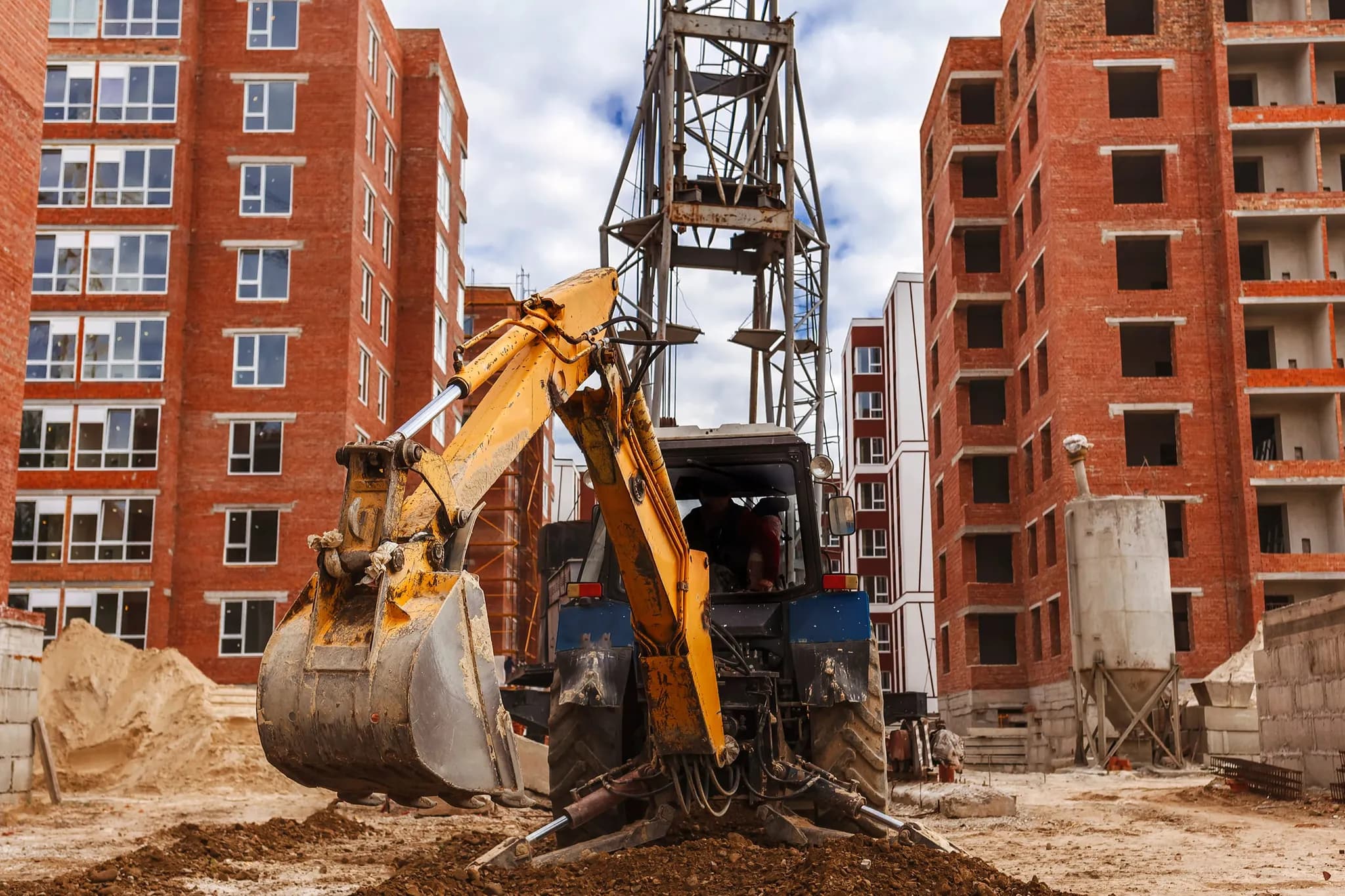 An excavator preparing ground beside a red-brick residential building