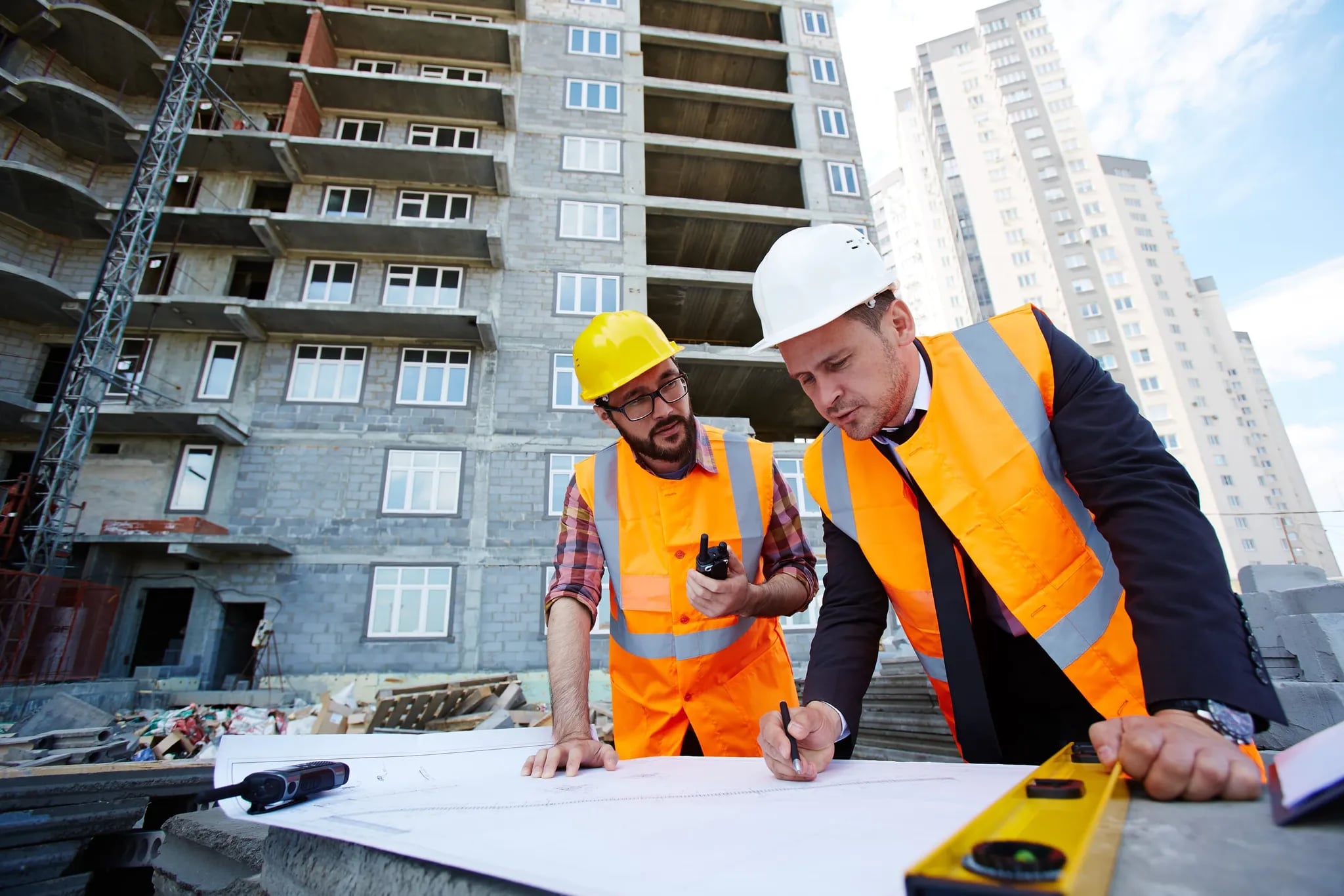 Two engineers in hard hats reviewing site plans and pointing at the build